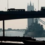 Tampak Tower Bridge dari kejauhan di London dengan kapal perang besar berlabuh di Sungai Thames. Siluet bus bertingkat di atas jembatan menonjolkan identitas khas kota. Atmosfer kabut menambah kesan dramatis, mencerminkan aspek historis dan strategis London, (7/1/2025). (nt/ho)