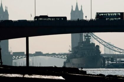 Tampak Tower Bridge dari kejauhan di London dengan kapal perang besar berlabuh di Sungai Thames. Siluet bus bertingkat di atas jembatan menonjolkan identitas khas kota. Atmosfer kabut menambah kesan dramatis, mencerminkan aspek historis dan strategis London, (7/1/2025). (nt/ho)