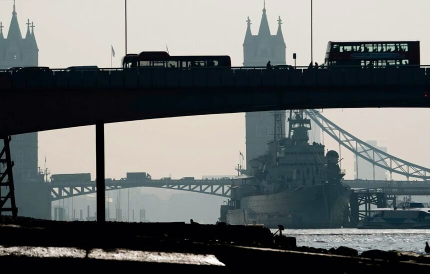 Tampak Tower Bridge dari kejauhan di London dengan kapal perang besar berlabuh di Sungai Thames. Siluet bus bertingkat di atas jembatan menonjolkan identitas khas kota. Atmosfer kabut menambah kesan dramatis, mencerminkan aspek historis dan strategis London, (7/1/2025). (nt/ho)