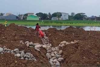 Keterangan Foto: Pekerja terlihat berada di atas tumpukan tanah dan batu yang menimbun saluran irigasi di kawasan proyek Namiland Tahap 3, Desa Kanjilo, Kecamatan Barombong, Kabupaten Gowa (23 Juni 2025). Penimbunan ini menuai kritik karena mengancam keberlangsungan pertanian warga yang bergantung pada aliran air dari saluran tersebut.