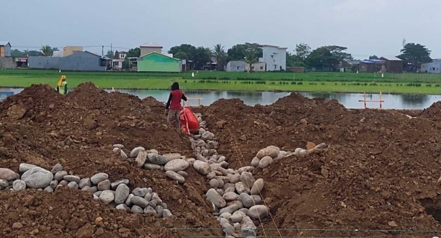 Keterangan Foto: Pekerja terlihat berada di atas tumpukan tanah dan batu yang menimbun saluran irigasi di kawasan proyek Namiland Tahap 3, Desa Kanjilo, Kecamatan Barombong, Kabupaten Gowa (23 Juni 2025). Penimbunan ini menuai kritik karena mengancam keberlangsungan pertanian warga yang bergantung pada aliran air dari saluran tersebut.