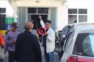 Seorang orator dari Aliansi Pemuda dan Masyarakat Tallo menyuarakan tuntutan di depan kantor CV. Kreatif Pisang Indonesia, BROWCYL, di Jalan Insinyur Juanda, Makassar (28/7/2025). Aksi ini menyoroti dugaan pelanggaran zonasi pergudangan di kawasan permukiman.