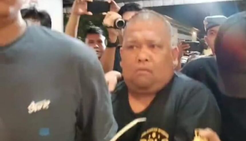 Samsul Tarigan saat digiring petugas, dikerumuni wartawan dan aparat keamanan. Meski Mahkamah Agung telah menjatuhkan vonis 1 tahun 4 bulan penjara sejak Juni 2025, eksekusi terhadap Samsul belum juga dilakukan oleh Kejari Binjai.