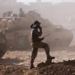 Seorang prajurit dengan alat komunikasi tampak di tengah debu tebal saat kendaraan lapis baja bergerak di pinggiran Kota Gaza, menandai dimulainya operasi darat IDF untuk merebut benteng Hamas.