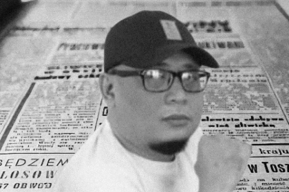 Seorang jurnalis berpose di depan latar koran lawas, simbol kerja investigasi yang menuntut ketelitian, keberanian, dan dedikasi dalam mengungkap kebenaran.
