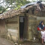 Seorang warga Aceh duduk di depan rumahnya yang tidak layak huni — potret nyata kesenjangan di tengah tanah yang kaya sumber daya alam.