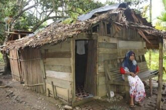 Aceh Kaya Raya, Rakyat Masih Hidup di Rumah Tak Layak Huni 21 Seorang warga Aceh duduk di depan rumahnya yang tidak layak huni — potret nyata kesenjangan di tengah tanah yang kaya sumber daya alam.