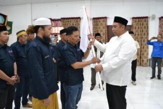 Bupati Maros menyerahkan bendera pataka kepada Ketua SMSI Maros usai prosesi pelantikan pengurus di Kantor PPK Maros, Ahad (1/3/2026).